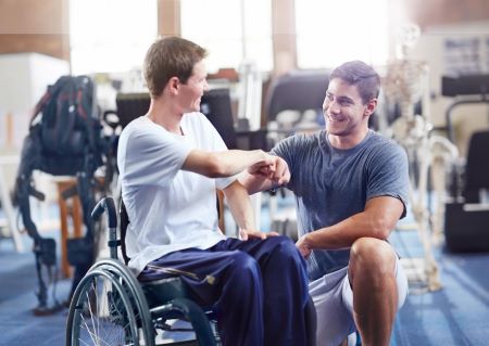 En man i rullstol gör en "fist-bump" med en annan man som står på knä bredvid mannen i rullstol. 